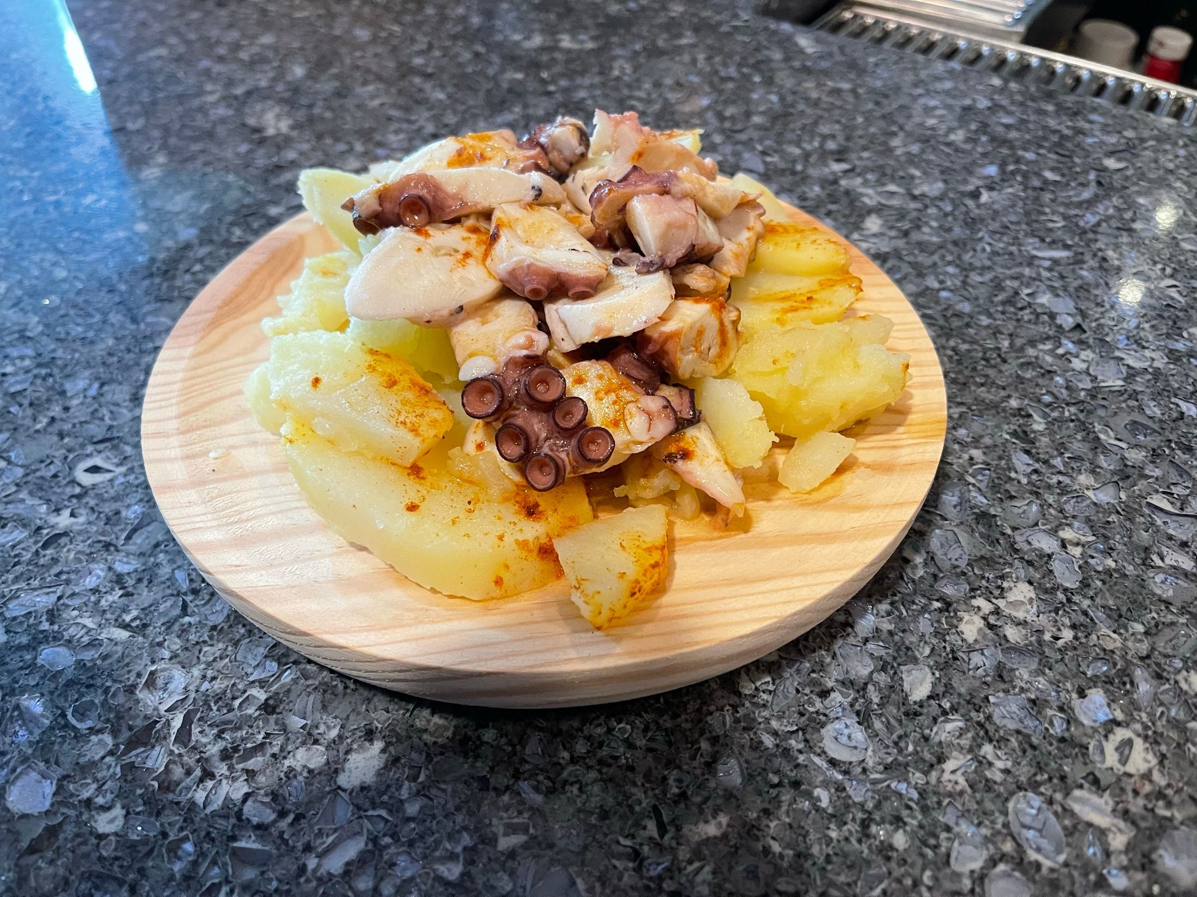 Pulpo a feria: octopus with paprika over steamed potatoes on a wooden plate